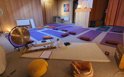 La salle préparée pour une séance : tapis, coussins et un gong posés au sol