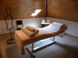Une table de massage garnie de serviettes roulées, dans une pièce mansardée en bois