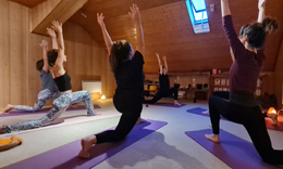 Quatre personnes en fente, bras levés, sur des tapis violets sous les poutres